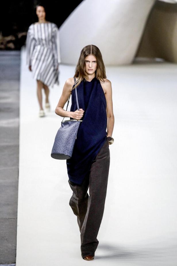 Eine Frau läuft auf einem Laufsteg mit einem blauen Kleid und einer passenden Handtasche.