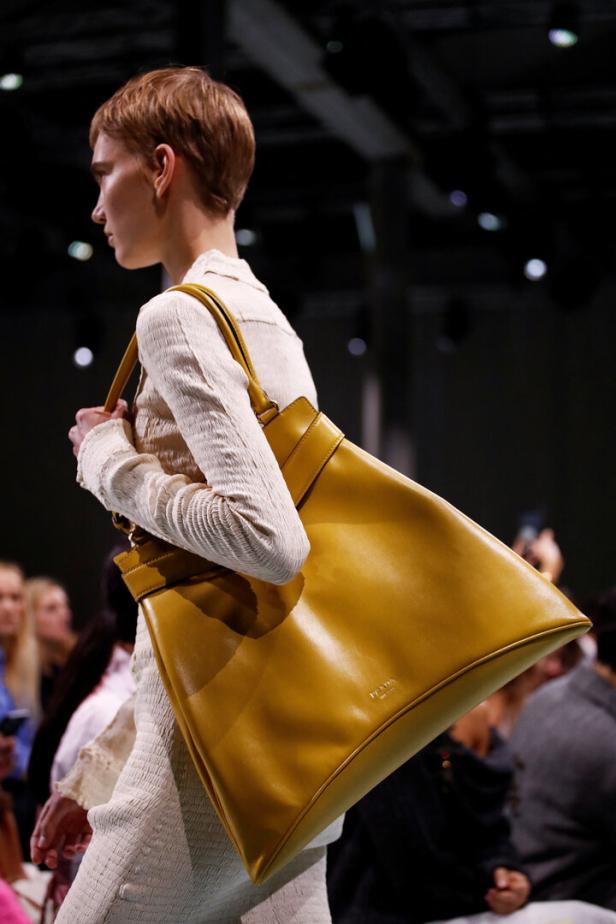 Ein Model präsentiert eine große, ockerfarbene Ledertasche von Prada auf dem Laufsteg.