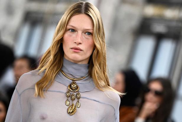 Eine blonde Frau mit einem goldenen Halsband mit Anhänger.
