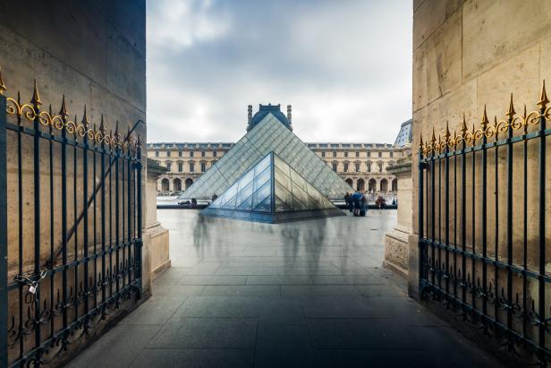 Blick durch ein Tor auf die Glaspyramide des Louvre in Paris.
