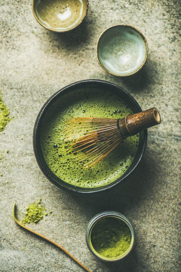 Eine Schale Matcha-Tee mit einem Bambusbesen auf einem grauen Untergrund.