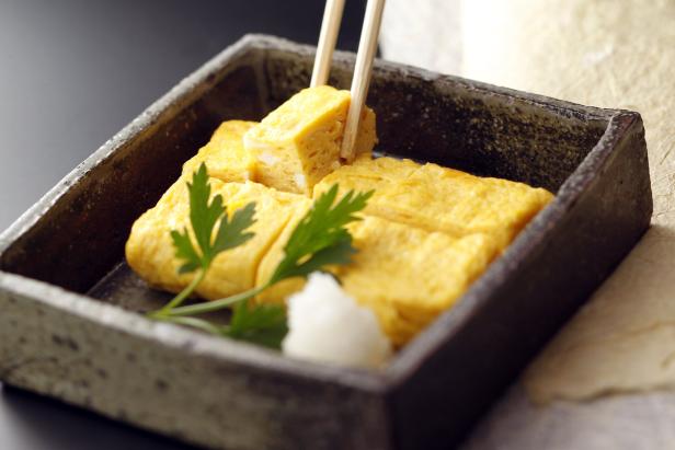 Tamagoyaki, ein japanisches Omelett, wird mit Stäbchen aus einer Schale gehoben.