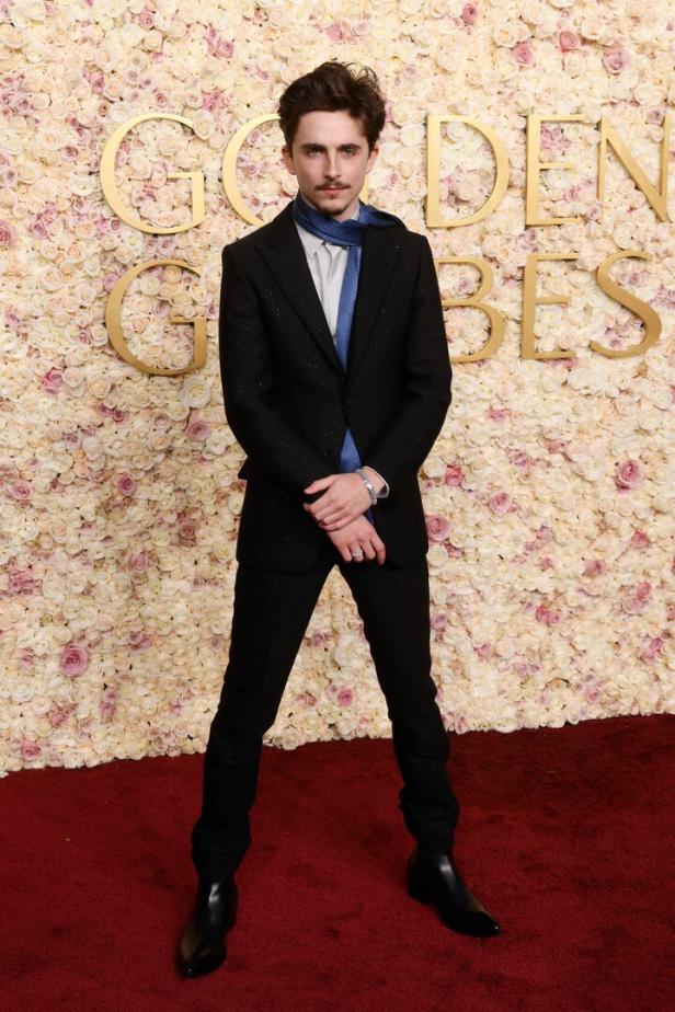 Timothée Chalamet posiert auf dem roten Teppich vor einer Wand aus Rosen bei den Golden Globes.