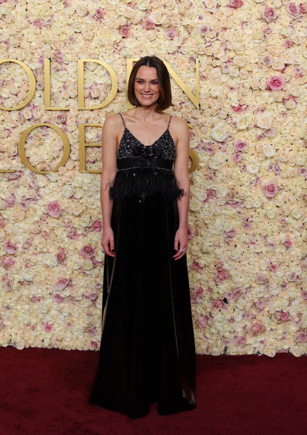 Eine Frau in einem schwarzen Kleid posiert vor einer Wand aus Rosen bei den Golden Globes.