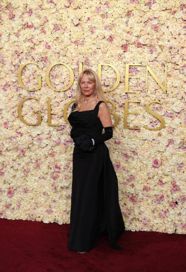 Eine Frau in einem schwarzen Kleid posiert vor einer Wand aus Rosen bei den Golden Globes.