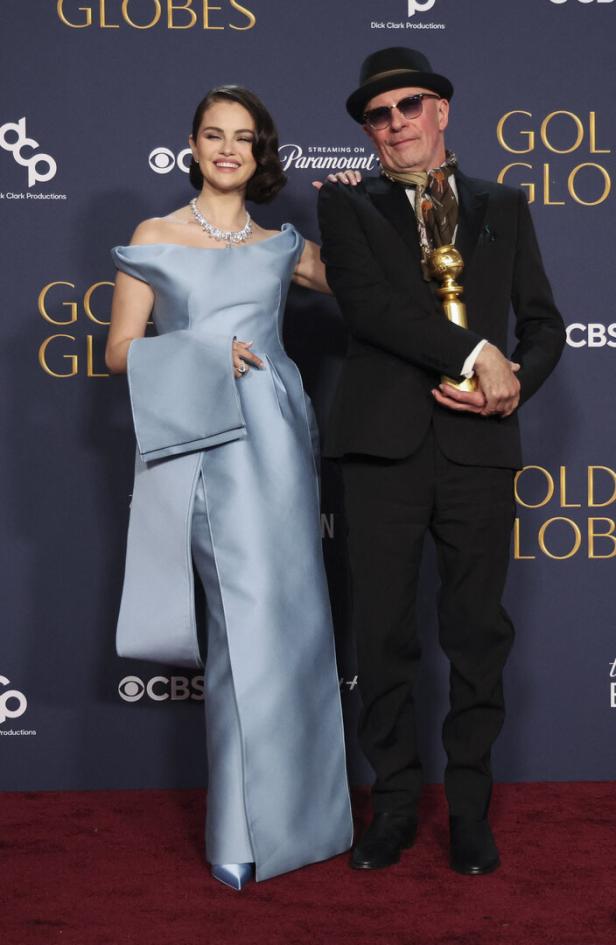 Selena Gomez und ein Mann mit Hut posieren mit einem Golden Globe Award auf dem roten Teppich.