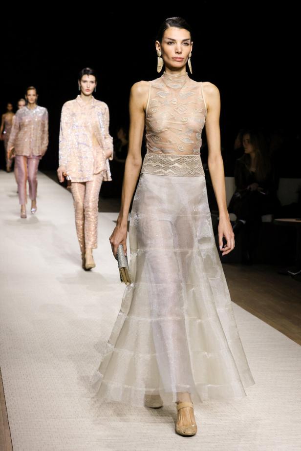 Eine Frau in einem transparenten, bodenlangen Kleid auf einem Laufsteg.