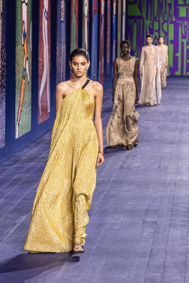 Eine Frau in einem goldenen Kleid auf dem Laufsteg bei einer Modenschau.