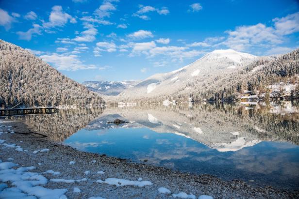 Ein Bergsee spiegelt die schneebedeckten Berge und den blauen Himmel wider.