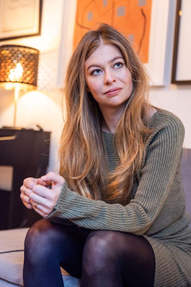 Zoë sitzt in einem grünen Kleid und schwarzen Strumpfhosen auf einem Sofa.