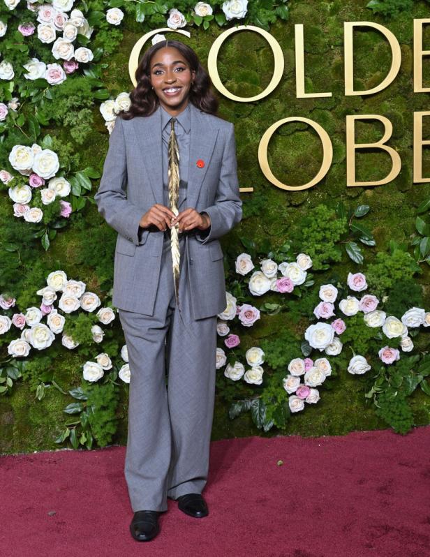 Eine Frau in einem grauen Anzug posiert vor einer Wand mit Blumen und dem Schriftzug „Golden Globes“.