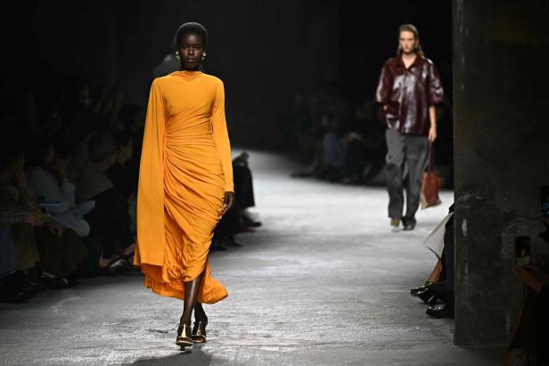 Eine Frau in einem orangefarbenen Kleid läuft auf einem Laufsteg.