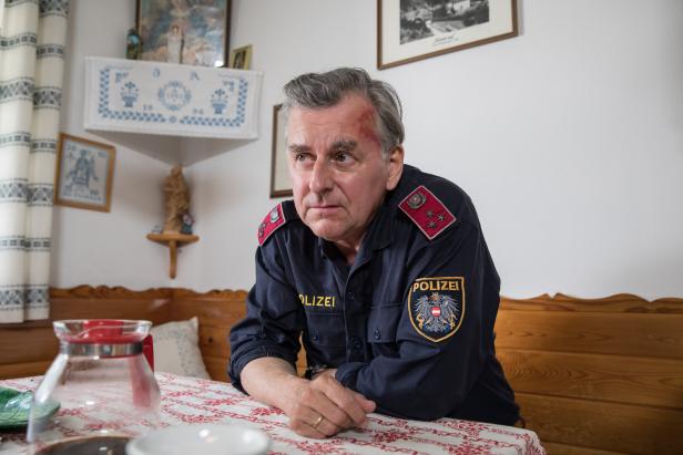 Ein Polizist mit einer Verletzung an der Stirn sitzt an einem Tisch.