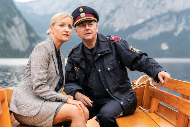 Eine Frau im Kostüm und ein Polizist sitzen in einem Boot auf einem See.