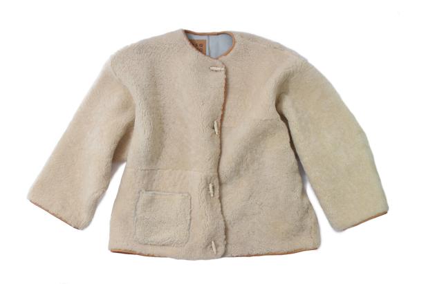 Eine beige Jacke aus Teddyfell mit Knebelknöpfen liegt vor einem weißen Hintergrund.
