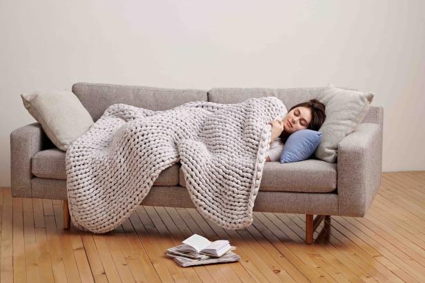 Eine Frau schläft auf einem grauen Sofa unter einer dicken, weißen Decke.
