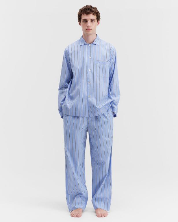 Ein Mann steht barfuß in einem blau-weiß gestreiften Pyjama vor einem weißen Hintergrund.