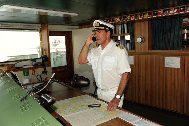 Das Traumschiff Ein Kapitän in Uniform telefoniert auf der Brücke eines Schiffes.