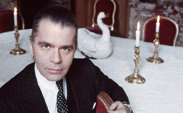 Karl Lagerfeld sitzt an einem Tisch mit Kerzenleuchtern und einer Schwanenfigur.