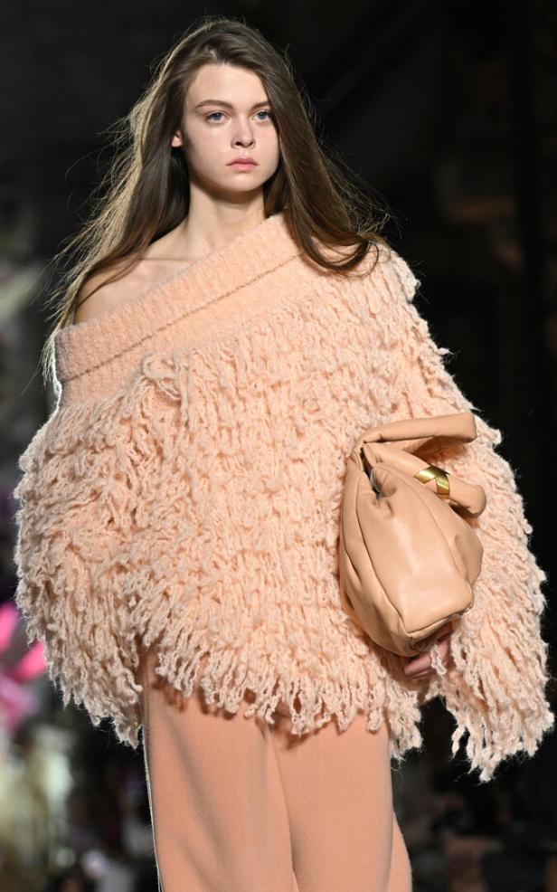 Ein Model präsentiert ein Outfit mit einem Fransenumhang und einer Handtasche in Peach-Farben.