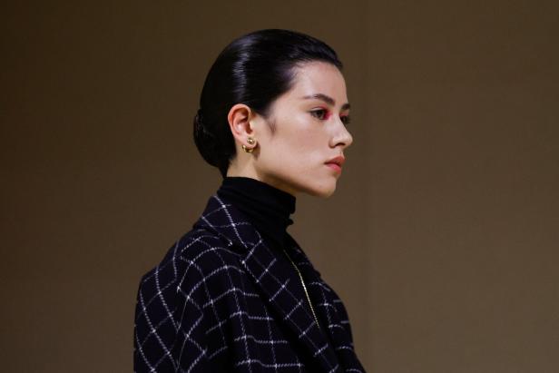 Eine Frau mit Dutt trägt einen karierten Blazer und auffälliges pinkes Augen-Make-up.