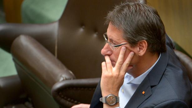Ein Mann mit Brille und Anzug sitzt nachdenklich in einem Sessel.