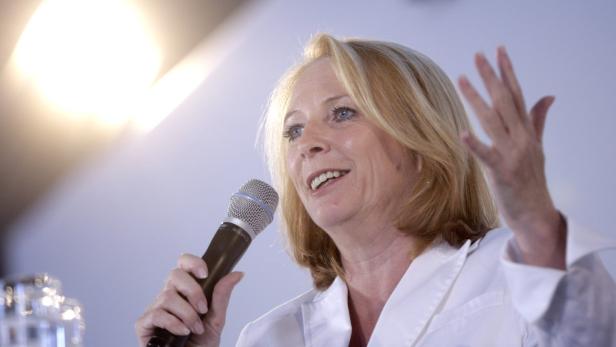 Eine Frau mit blonden Haaren spricht in ein Mikrofon und gestikuliert mit der Hand.
