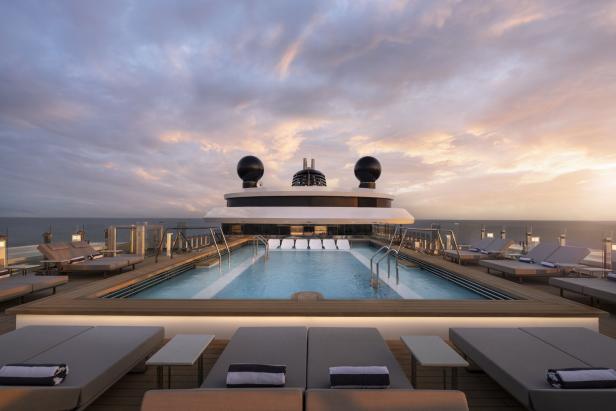 Ein Pooldeck auf einem Kreuzfahrtschiff mit Liegestühlen und Blick auf das Meer bei Sonnenuntergang.