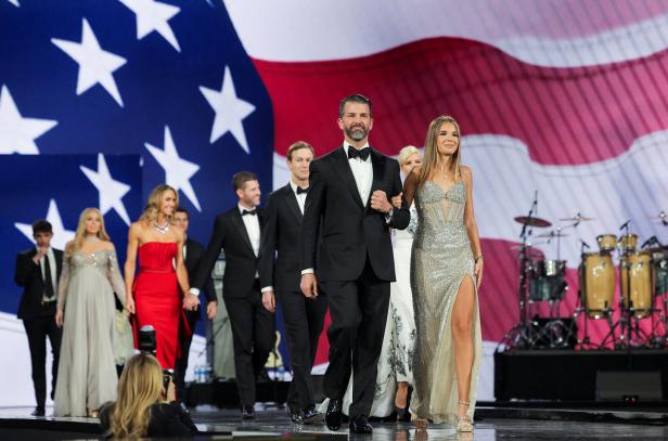 Donald Trump Jr. und Kimberly Guilfoyle führen eine Gruppe von Personen vor einer großen US-Flagge an.