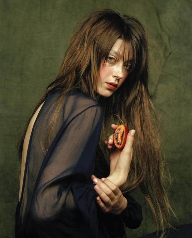 Eine Frau mit langen braunen Haaren hält eine aufgeschnittene Tamarillo in der Hand.