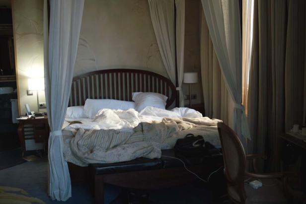 Ein Himmelbett mit zerwühlter Bettwäsche in einem dunklen Raum.
