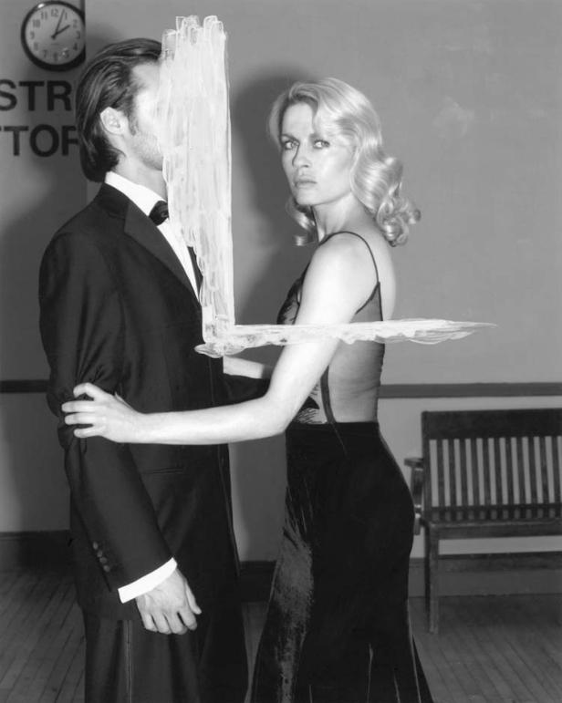 Eine Frau im Abendkleid mit einem Mann im Smoking, dessen Gesicht teilweise verdeckt ist.