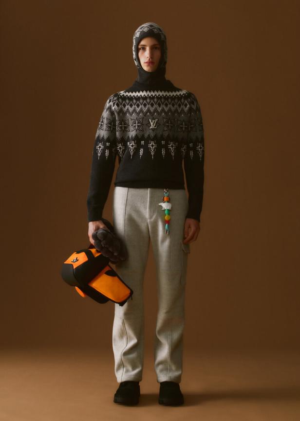 Ein Mann in einem Louis Vuitton-Pullover und einer Sturmhaube hält eine orangefarbene Tasche.