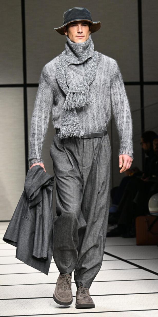 Ein Mann in einem grauen Wollpullover, einer Hose und einem Hut auf einem Laufsteg.
