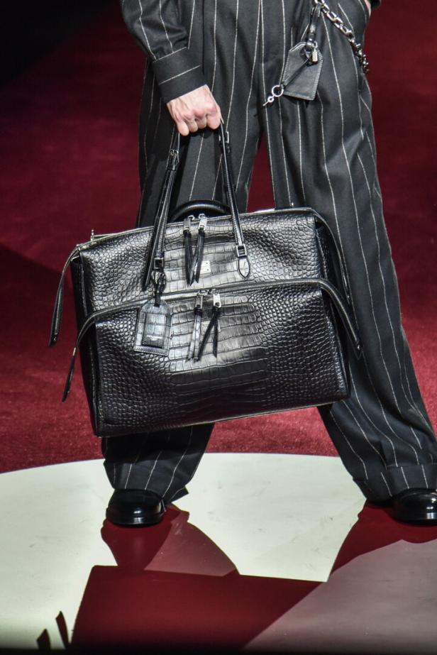 Ein Model trägt eine schwarze Krokodilledertasche und einen gestreiften Anzug auf dem Laufsteg.