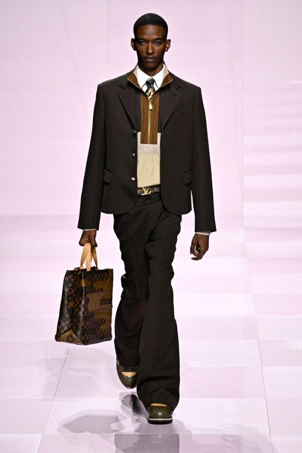 Ein Mann in einem braunen Anzug mit einer Louis Vuitton Tasche auf einem Laufsteg.