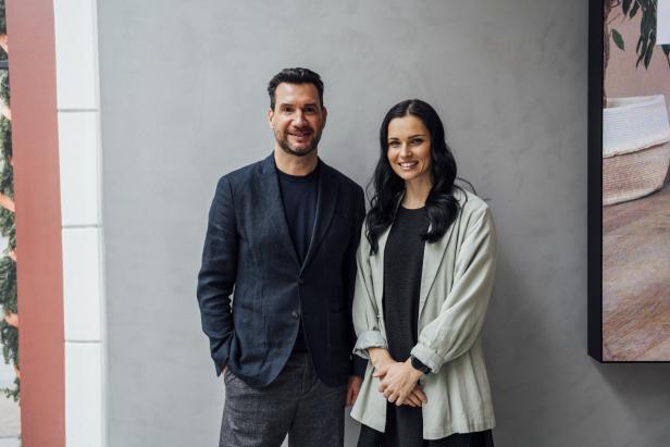 Ein Mann und eine Frau stehen lächelnd vor einer grauen Wand.