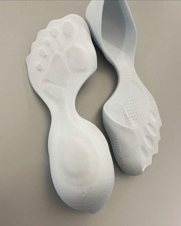 Zwei weiße Balenciaga-Schuhe mit Fußabdruck-Design stehen auf einem Tisch.