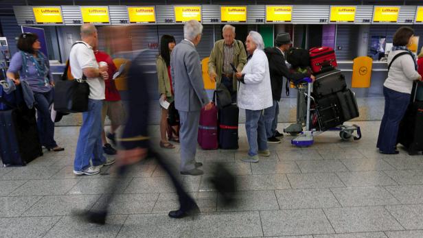 Reisende stehen mit Gepäck an den Lufthansa-Check-in-Schaltern.
