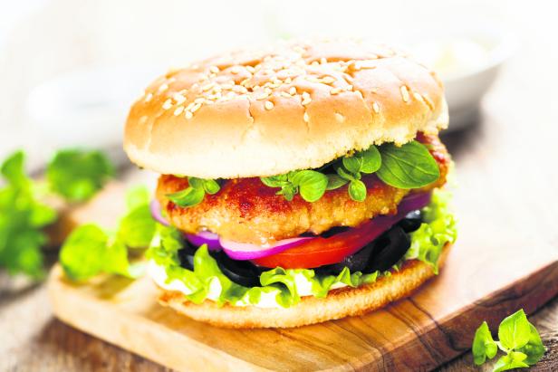 Ein appetitlicher Burger mit Salat, Tomaten, Zwiebeln und einem Fleisch-Patty auf einem Holzbrett.