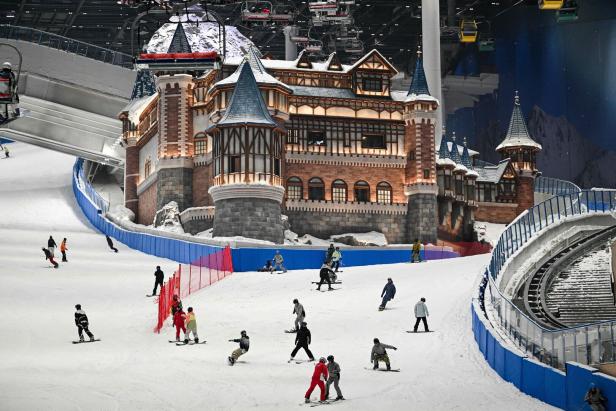 Wintersportler fahren auf einer Piste in einer Halle hinab. Mitten auf dem Hügel steht ein künstliches Schloss.