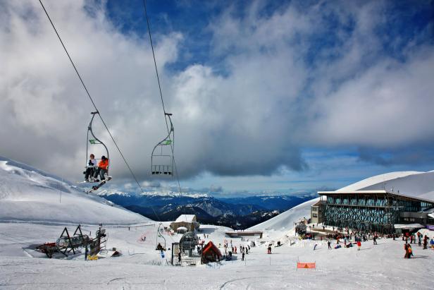 Ein Sessellift im Gebirge mit einem Panoramarestaurant daneben.