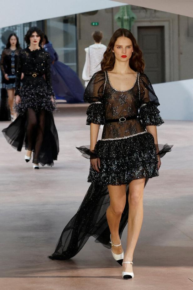 Models präsentieren transparente, schwarze Kleider auf einem Laufsteg.