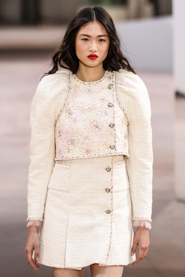 Eine Frau präsentiert ein zweiteiliges Tweed-Ensemble mit Puffärmeln und silbernen Knöpfen.