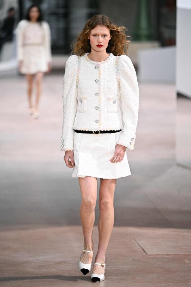 Ein Model präsentiert ein weißes Tweed-Kostüm mit Puffärmeln und passenden Schuhen auf dem Laufsteg.