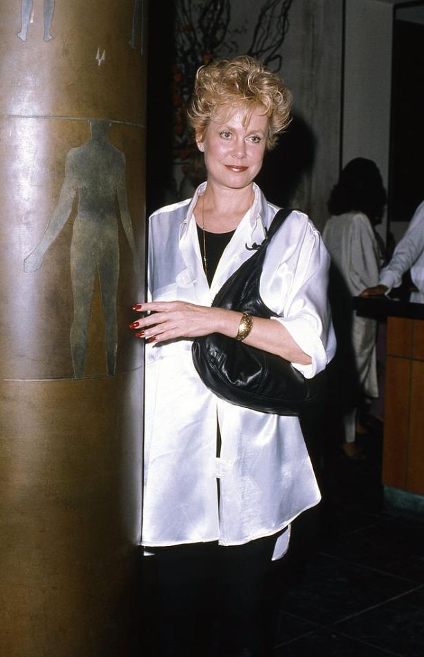 Eine Frau mit blonden Haaren posiert neben einer Säule mit einer menschlichen Figur.