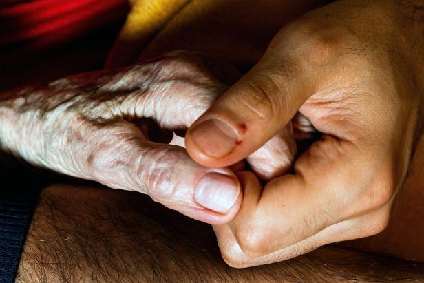 Eine junge Hand hält die Hand einer älteren Person.