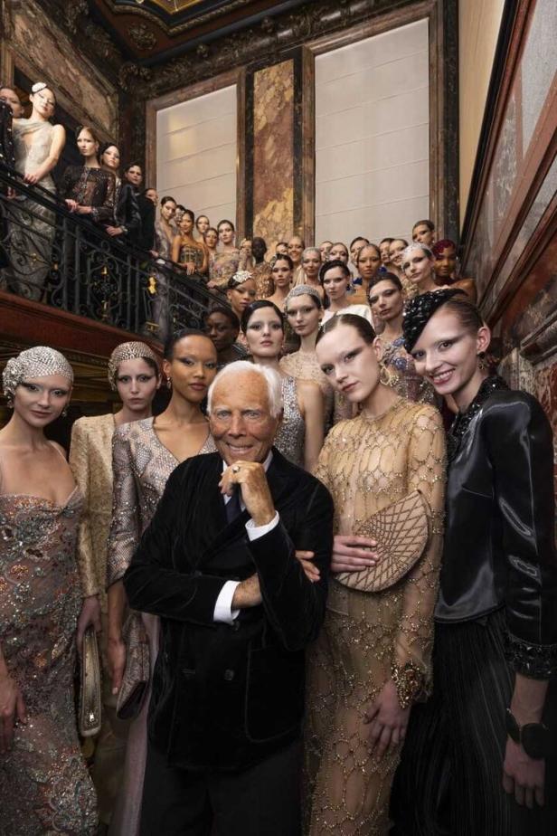 Giorgio Armani posiert mit einer Gruppe von Models auf einer Marmortreppe.