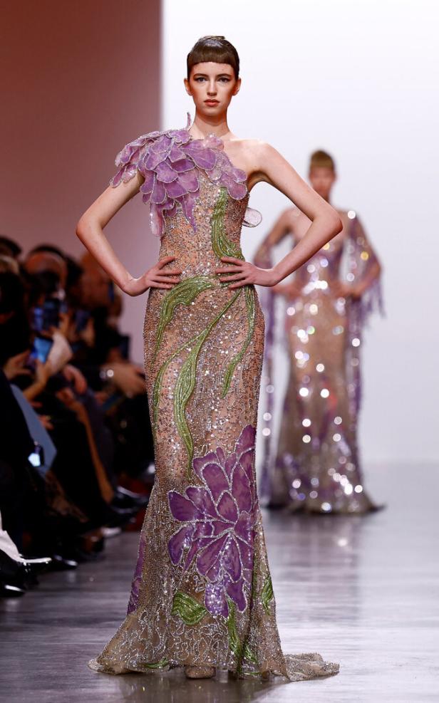Ein Model präsentiert ein bodenlanges, mit Blumenmustern verziertes Kleid auf dem Laufsteg.