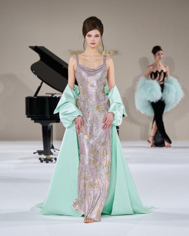 Eine Frau in einem glitzernden Kleid mit Blumenmuster und einem mintgrünen Überwurf auf einem Laufsteg.
